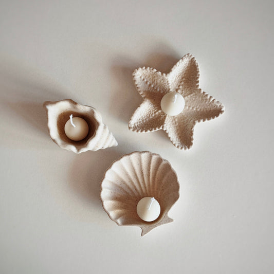 Three jesmonite candle holders shaped like a shell, a star, and a circle with small candles inside on a light gray background.
