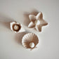 Three jesmonite candle holders shaped like a shell, a star, and a circle with small candles inside on a light gray background.